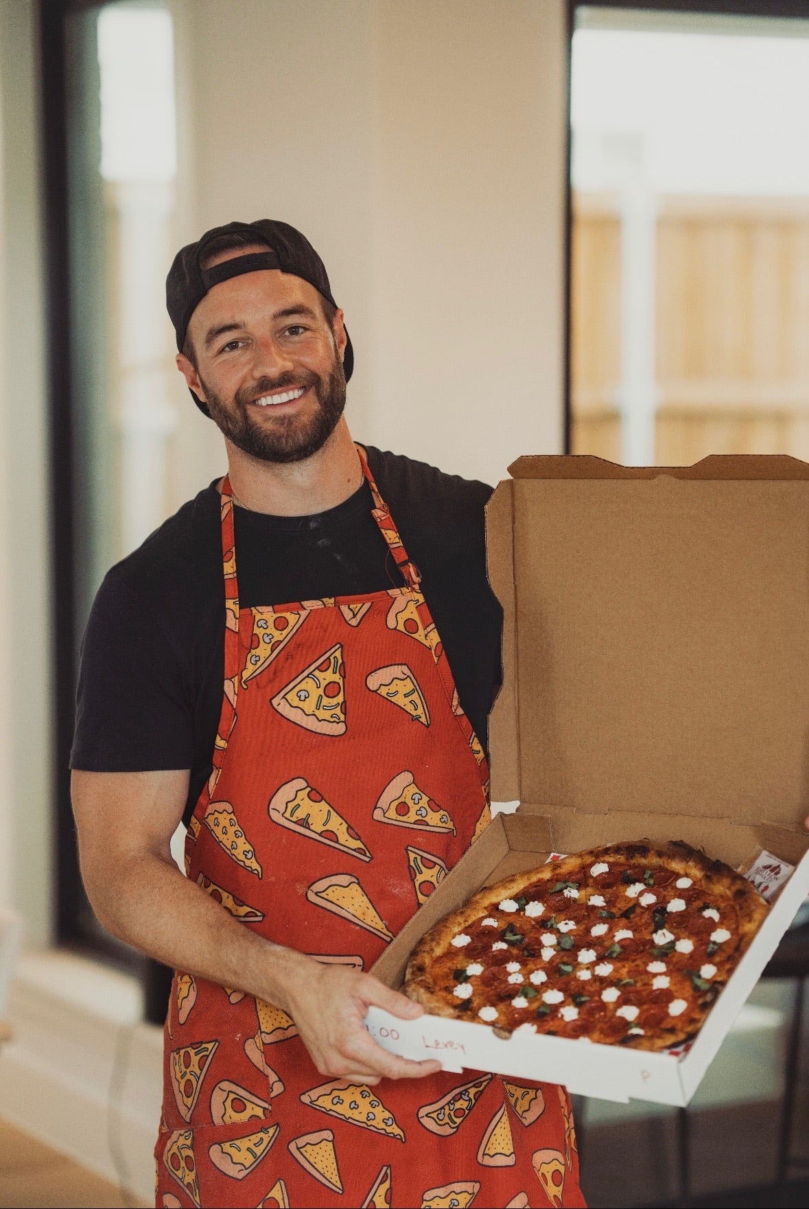 Dave in a pizza-themed apron holding a box of pizza